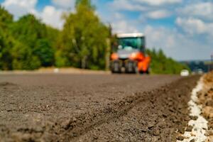 Roller is compacting asphalt on the road during the construction of the road on the background of blue sky. Compaction of the pavement in road construction. photo