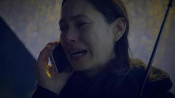 triste mujer hablando en célula teléfono fuera de a noche en lloviendo clima video