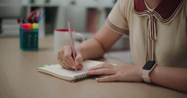 metraggio costante sparo, selettivo messa a fuoco, mani di giovane asiatico donna seduta a scrivania Tenere penna fabbricazione Appunti nel diario a casa, creativo pensieri per scrivere sul diario, idea e ispirazione video