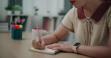 beeldmateriaal dolly schot, selectief focus, handen van jong Aziatisch vrouw zittend Bij bureau Holding pen maken aantekeningen in dagboek Bij huis, creatief gedachten naar dagboek bijhouden, idee en inspiratie video