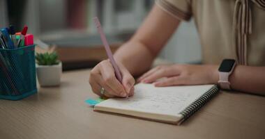 imágenes estable tiro, selectivo enfocar, manos de joven asiático mujer sentado a escritorio participación bolígrafo haciendo notas en diario a hogar, creativo pensamientos a diario, idea y inspiración video