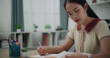 imágenes muñequita disparo, joven asiático mujer sentado a escritorio escritura información en diario cuaderno mientras leyendo libro a hogar, creativo pensamientos a diario, idea y inspiración video