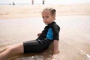 Little girl surfer in wetsuit lies ocean beach photo