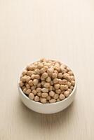 Chickpeas in a small white bowl on a wooden table. photo