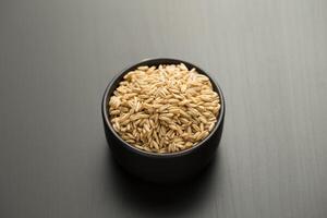 Oats rice in a small black bowl on a black wooden table. photo