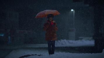 Jeune africain femme permanent sur rue à nuit pendant neige tomber avec parapluie video