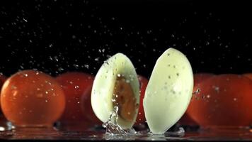 The boiled egg falls on the table and breaks down into halves. On a black background. Filmed is slow motion 1000 fps. video
