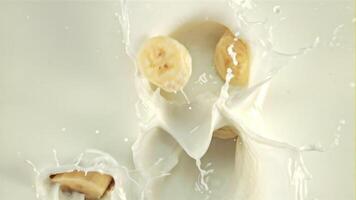 stukken van banaan vallen in de melk met spatten. Aan een wit achtergrond. gefilmd is langzaam beweging 1000 fps. video