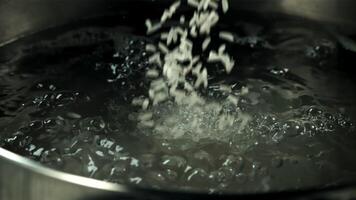 Raw rice falls into a pot of boiling water. Macro background. Filmed is slow motion 1000 fps. video