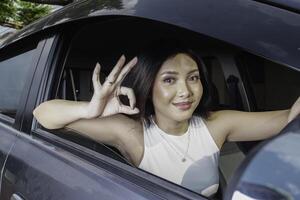 Attractive young Asian woman in casual wear gesturing OK sign with her fingers while driving a car photo