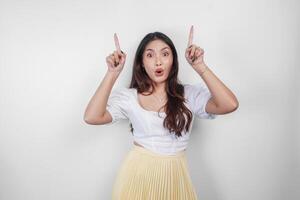 A shocked Asian woman, pointing to copy space above her, isolated by white background. photo