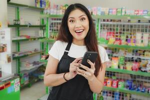 Shocked Asian woman as a cashier is wearing black apron and holding her phone photo