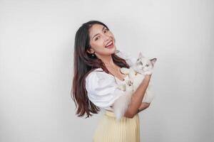 retrato de joven asiático mujer participación linda muñeca de trapo gato con azul ojos. hembra abrazando su linda largo pelo gatito aislado por blanco antecedentes. adorable Doméstico mascota concepto. foto