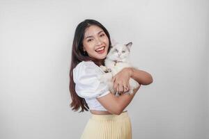 retrato de joven asiático mujer participación linda muñeca de trapo gato con azul ojos. hembra abrazando su linda largo pelo gatito aislado por blanco antecedentes. adorable Doméstico mascota concepto. foto