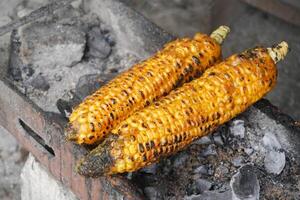 maduro amarillo maíz siendo A la parrilla en el reja con llameante carbón, Listo a atender. foto