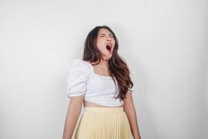 Portrait of sleepy attractive Asian woman wearing a dress, feeling tired after night without sleep, yawning with her mouth wide open photo