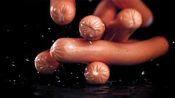 Fresh sausages fall on a wet black table. Filmed on a high-speed camera at 1000 fps. High quality FullHD footage video