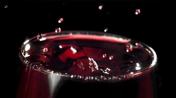 une laissez tomber chutes dans une verre de du vin. sur une noir Contexte. filmé sur une haute vitesse caméra à 1000 ips. haute qualité Full HD métrage video