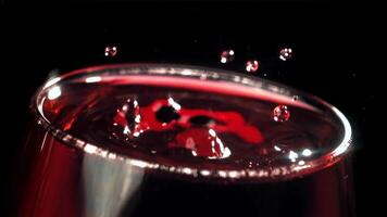 une laissez tomber chutes dans une verre de du vin. sur une noir Contexte. filmé sur une haute vitesse caméra à 1000 ips. haute qualité Full HD métrage video