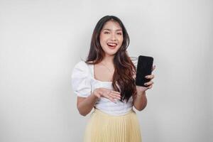 A cheerful Asian woman is smiling and holding her smartphone, isolated by white background. photo