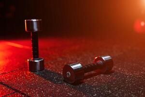 Heavy dumbbells on the floor. Modern dark gym with red light. Sports equipment. photo