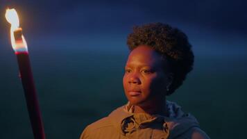 jovem africano mulher com encaracolado cabelo explorando Sombrio noite com tocha luz video