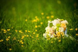 Wedding bouquet of tender light roses on grass in summer. Natural background of green grass with yellow wildflowers and fresh wedding bouquet. Space for text. photo