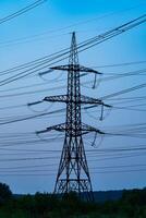 Single high voltage tower on the background of blue sky after sun set. Numerous wires of electricity power stations at the backdrop of twilight. Dark blue sky crossed by the heavy cables. photo