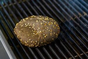 Brown bread for hamburger with sesame seeds is fried on the grill. Thin smoke coming from under the bun. Close-up. photo