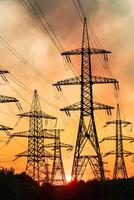 Last rays of the setting sun against the gigantic towers of transmission power lines. Dark thin smoke over the electrical equipment towers at the backdrop of pink and yellow sky. photo