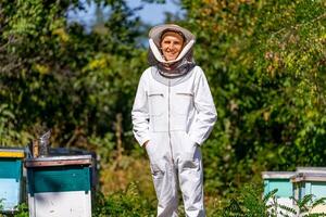 Agricultural beekeeper in protective cloth posing for camera. Man examining hives in summer. photo