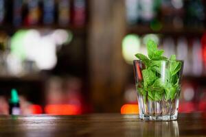 a glass with mint stands on a wooden rack in the bar on the background of the interior. Close-up photo