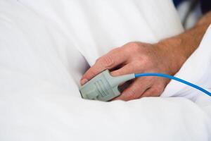 Patient's Hand with Pulse Oximeter on Finger for Monitoring in modern Hospital. Closeup. photo