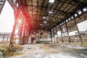 Abandoned ruined industrial warehouse or factory building inside, corridor view with ruins and pitted roof. Old industrial factory for demolition. Destroyed factory photo