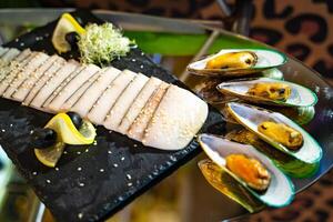 An appetizing photo of some exotic meat cutted in slices with lemon and olives and oysters on the glass table. Banquet in a restaurant.