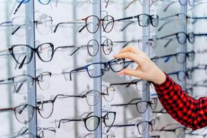 Eyeglasses shop. Stand with glasses in the store of optics. Woman's hand chooses glasses. photo