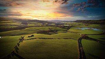 Aerial view of a lush green countryside at sunset with rolling hills, fields, and a winding river. photo