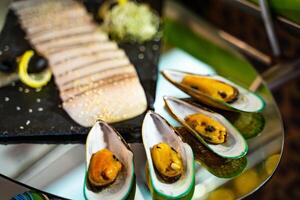 Seafood. Baked oysters in shells and sliced exotic meat on a glass table. Appetizer for guests on a decorated table. Close-up. photo