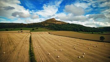 Scenic view of a harvested field with hay bales and a majestic hill under a cloudy sky in Yorkshire Moors. photo