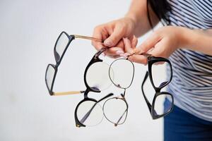 woman shows four pairs of eyeglasses to choose from on a white background in the studio. Close-up photo