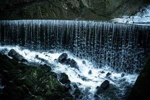 A serene waterfall cascading over a rocky cliff into a turbulent pool below. photo