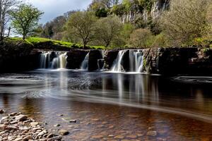 Tranquil waterfall with smooth flowing water in a lush green landscape, under a clear sky in Yorkshire Dales. photo