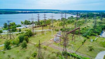 Top view of electricity pylons and high-voltage power lines on the green grass on the background of the river. Power plant. Electrical Power Grid. Aerial view photo