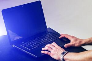 Cropped image of a young man working on his laptop at the table. Rear view of business man hands busy using laptop at office desk, young male typing on computer. Selective focus. Closeup. photo