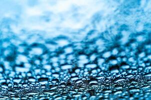 Fantastic view of clear big and small raindrops on a glass on blue background. Realistic pure water droplets condensed for creative design. Macro shot photo