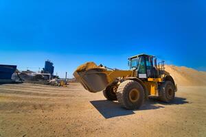 The tractor collects a scoop with gravel. excavator extracts sand and gravel for the concrete mix. Blue sky above. photo