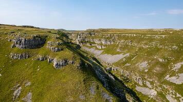 Aerial view of a lush green limestone valley with rocky cliffs under a clear blue sky. photo