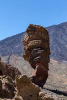 Unique rock formation stands against a clear blue sky with rugged mountains in the background in the Teide, National Park, Tenerife photo