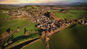 Aerial view of a quaint village surrounded by green fields and trees with a scenic landscape in the background. photo