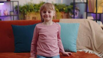 retrato de pequeño niño niña niño solo en sofá a hogar demostración Okay gesto, me gusta firmar, positivo bueno video